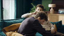 two men are sitting on a blue couch and one of them has his hand on the other 's ear