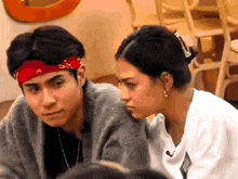 a man with a red bandana on his head looks at a woman in a white shirt