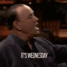 a man in a suit is saying it 's wednesday in a bar .