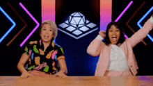 two women are sitting at a table with their arms in the air .
