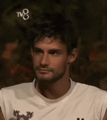 a man with a beard is wearing a white shirt without sleeves and looking at the camera .