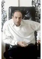 a man in a white shirt is sitting in a chair with the number 100 on the bottom right