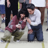 a man and a woman are posing for a picture in a crowd with korean writing behind them