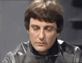 a close up of a man wearing a black leather jacket with his eyes closed .