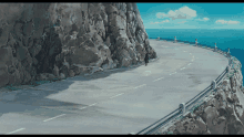 a road with a rocky cliff on the side and a body of water in the background