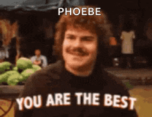 a man with a mustache is standing in front of a fruit stand and says `` you are the best '' .