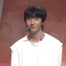 a young man wearing a white shirt and a microphone around his neck is looking at the camera .