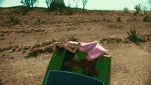 a woman in a pink dress laying on top of a green car