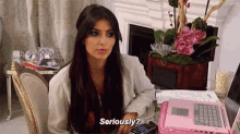 a woman is sitting at a table with a laptop and a cell phone and says `` seriously '' .
