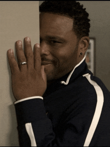 a man with a ring on his finger peeking behind a wall