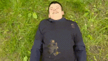 a young boy is laying in the grass with a squirrel stuck to his shirt .