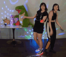 two girls are dancing in front of a stuffed dinosaur and a table