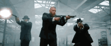 three men in suits and hats are holding guns in a dark room