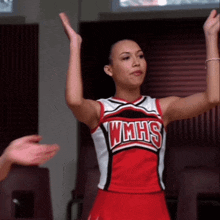 a cheerleader wearing a wmhs uniform holds her hands in the air