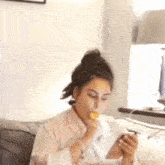 a woman is sitting on a couch eating a piece of food while looking at her phone .