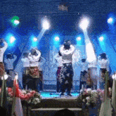 a group of people are dancing on a stage in front of a blue background