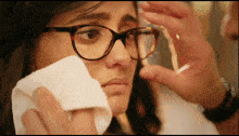 a woman wearing glasses wipes her face with a napkin