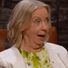 a woman with a surprised look on her face is wearing a white jacket and green dress .