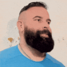 a man with a beard wears a blue shirt and a chain around his neck