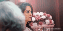 a woman is standing in front of a vase of flowers and looking at something .