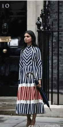 the woman is wearing a striped dress and holding an umbrella .