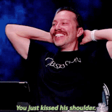 a man wearing a black shirt that says obsession is laughing