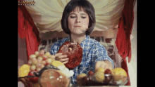 a woman in a plaid shirt is eating a piece of meat next to a bowl of fruit