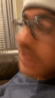 a man wearing glasses and a beanie is sitting on a couch making a funny face .