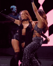 two women are dancing on a stage with their arms in the air