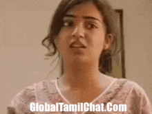 a woman is standing in front of a wall with the website globaltamilchat.com written in the corner