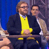 a man with glasses and a yellow sweater sits at a table
