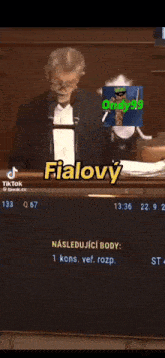 a man in a tuxedo is giving a speech in front of a microphone with mimon written on the screen
