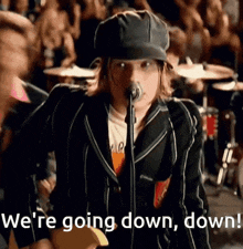 a woman singing into a microphone with the words " we 're going down down " behind her