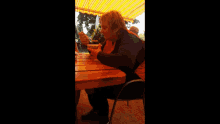 a woman sits at a table under a yellow awning