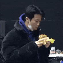a young man wearing a mask is eating a sandwich