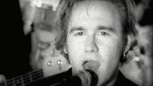a black and white photo of a man singing into a microphone while holding a guitar .