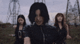 three women are standing in a field with one wearing a leather jacket
