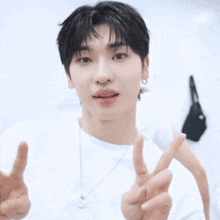 a young man wearing a white shirt and a silver necklace is giving a peace sign .