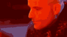 a bald man is smiling and looking at the camera in a red and blue light .