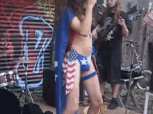 a woman in a wonder woman costume is singing into a microphone while a man plays a guitar behind her .