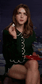 a woman in a green sweater is sitting on a chair eating a piece of cake