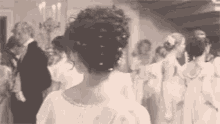 a woman in a white dress is standing in front of a crowd of people at a party .