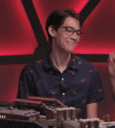 a man wearing glasses and a blue shirt is laughing while a woman feeds him with chopsticks