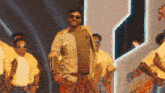 a man wearing sunglasses is standing in front of a group of men in yellow shirts