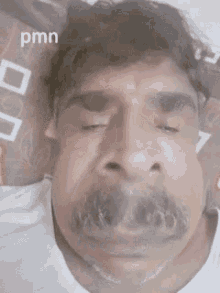 a man with a mustache is laying on a bed with his eyes closed and the word pmn on the bottom