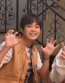 a young boy wearing a brown vest is making a funny face with his hands in the air .