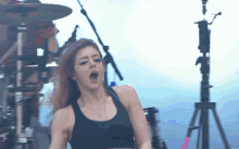 a woman in a black tank top is singing into a microphone on stage