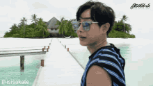 a man wearing sunglasses and a striped shirt is standing on a dock in front of a tropical island