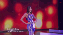 a woman is standing on a stage wearing a colombia sash and a blue dress .