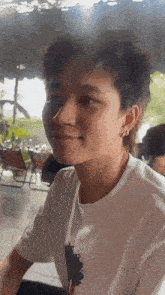 a young man wearing a white shirt and earrings looks at the camera .
